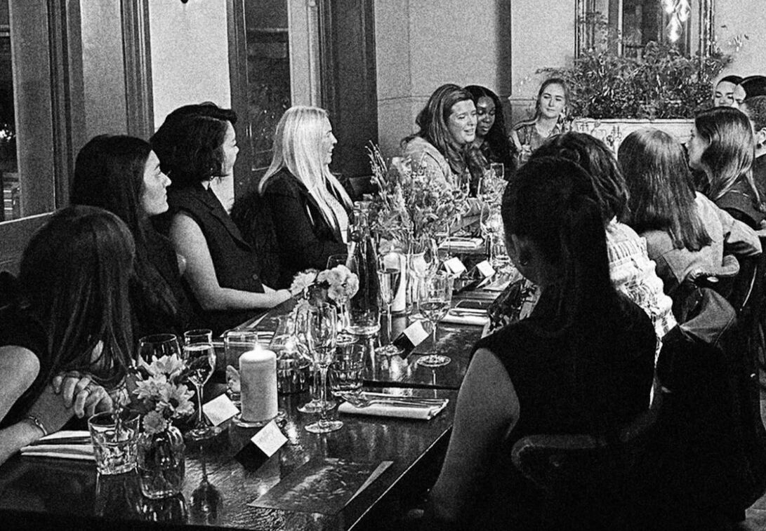 Black and white photograph showing a group of female AllSaints employees having dinner and talking.
