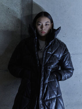 Woman wearing a leather puffer jacket leaning against a wall.