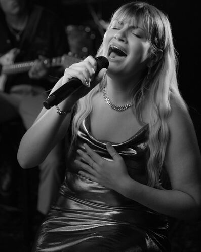 Maddie Zahm singt vor einem bunten Hintergrund in ein Mikrofon.