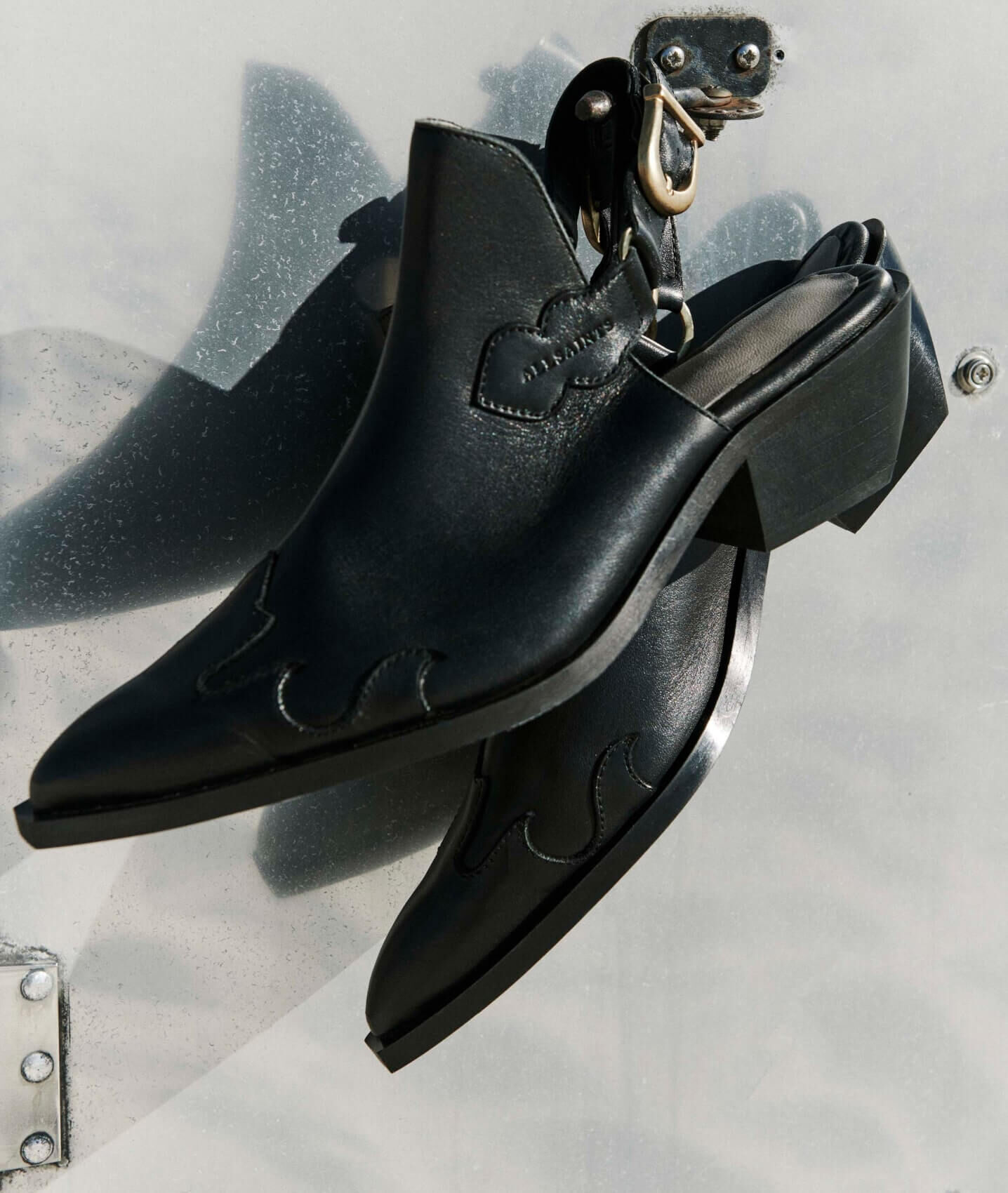 Closeup image of a pair of pointed black open back midi heels.