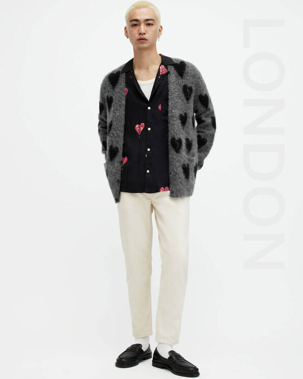 Portrait of a model wearing a dark grey cardigan with black heart motif and cream coloured corduroy jeans with leather loafers with LONDON written on the right hand side.