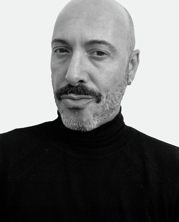 A black and white headshot of a man with a moustache wearing a black turtle neck