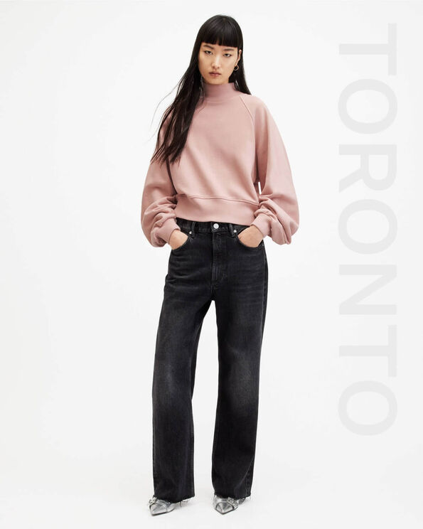 Portrait of a model wearing a light pink sweatshirt with black wide leg jeans with writing TORONTO on the right hand side.