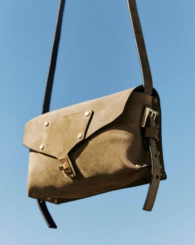 Un sac en cuir suédé marron clair avec des détails cloutés devant un ciel bleu.