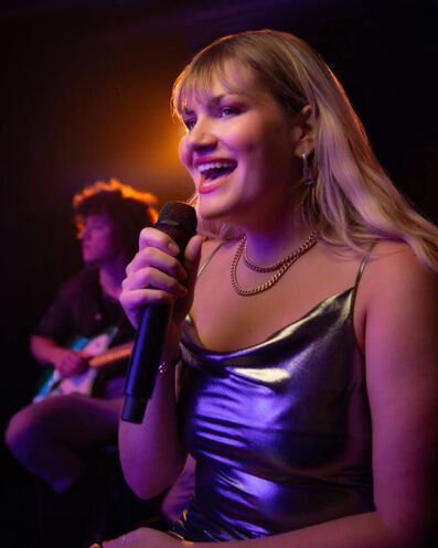 Gros plan de la chanteuse Maddie Zahm chantant dans un micro et souriant.