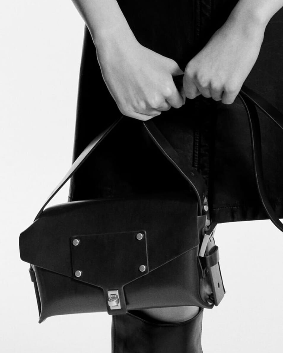 Black and white image of a person holding a black leather bag by the strap with both hands.