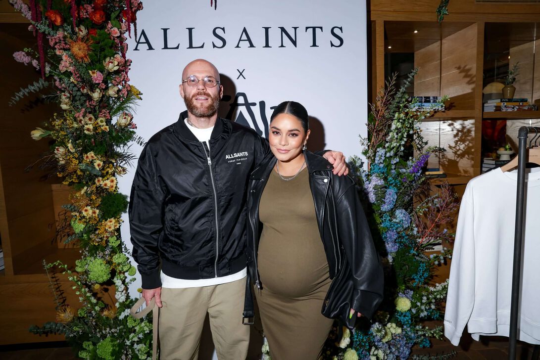 Photograph showing the interior of an AllSaints Store with Caliwater founder Vanessa Hudgens and Man posing infront of a AllSaints step and repeat.