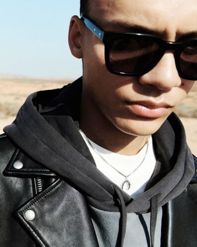 Closeup of a man wearing black sunglasses, a black leather jacket and black hoodie over a white t-shirt with a sterling silver necklace.