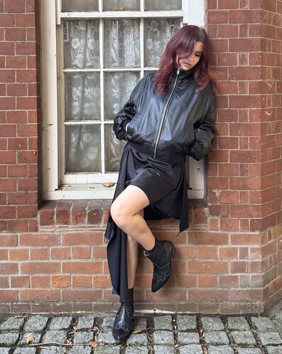 Woman standing against brick wall in leather jacket