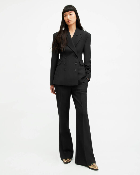 Portrait of a model wearing a black tailored blazer and black flared tailored trousers with cowboy leather boots with pointed golden tips.