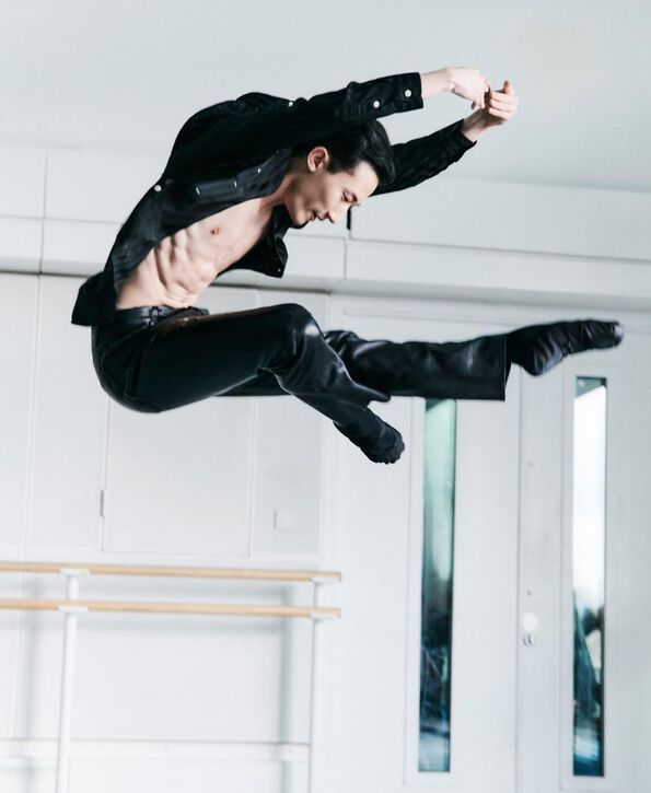 A man wearing an unbuttoned black shirt and black leather pants leaping.