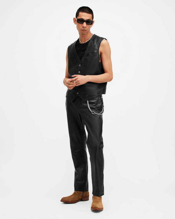 Portrait of a male model wearing a black leather waistcoat, black leather trousers and black sunglasses, with light brown suede boots.