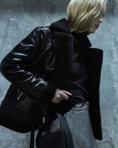 Woman wearing a black leather shearling jacket with silver skirt and black handbag