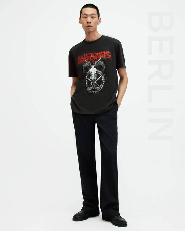 Porträt eines männlichen Models, das ein grafisches schwarzes T-Shirt mit schwarzen Jeans und schwarzen Lederstiefeln trägt und auf der rechten Seite der Schriftzug „BERLIN“ steht.