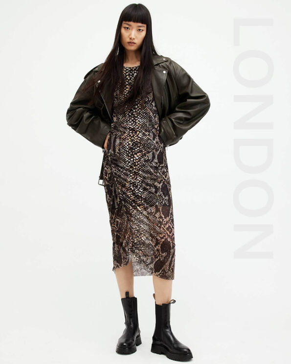 Portrait of a model wearing a dark green leather jacket with a mesh snake print dress and black leather boots with LONDON written on the right-hand side.