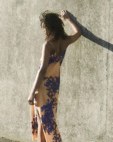 Woman wearing an orange slip dress with purple florals leaning on a concrete wall