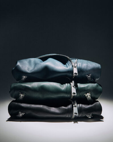 Gros plan sur une pile de vestes biker en cuir pliées couleur bleu, vert et noir.