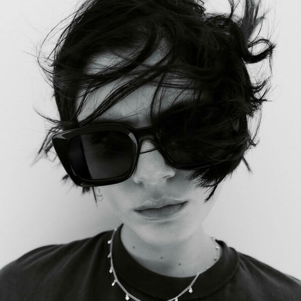 Black and white closeup photograph of a woman with short dark hair wearing sunglasses, a necklace and a t-shirt