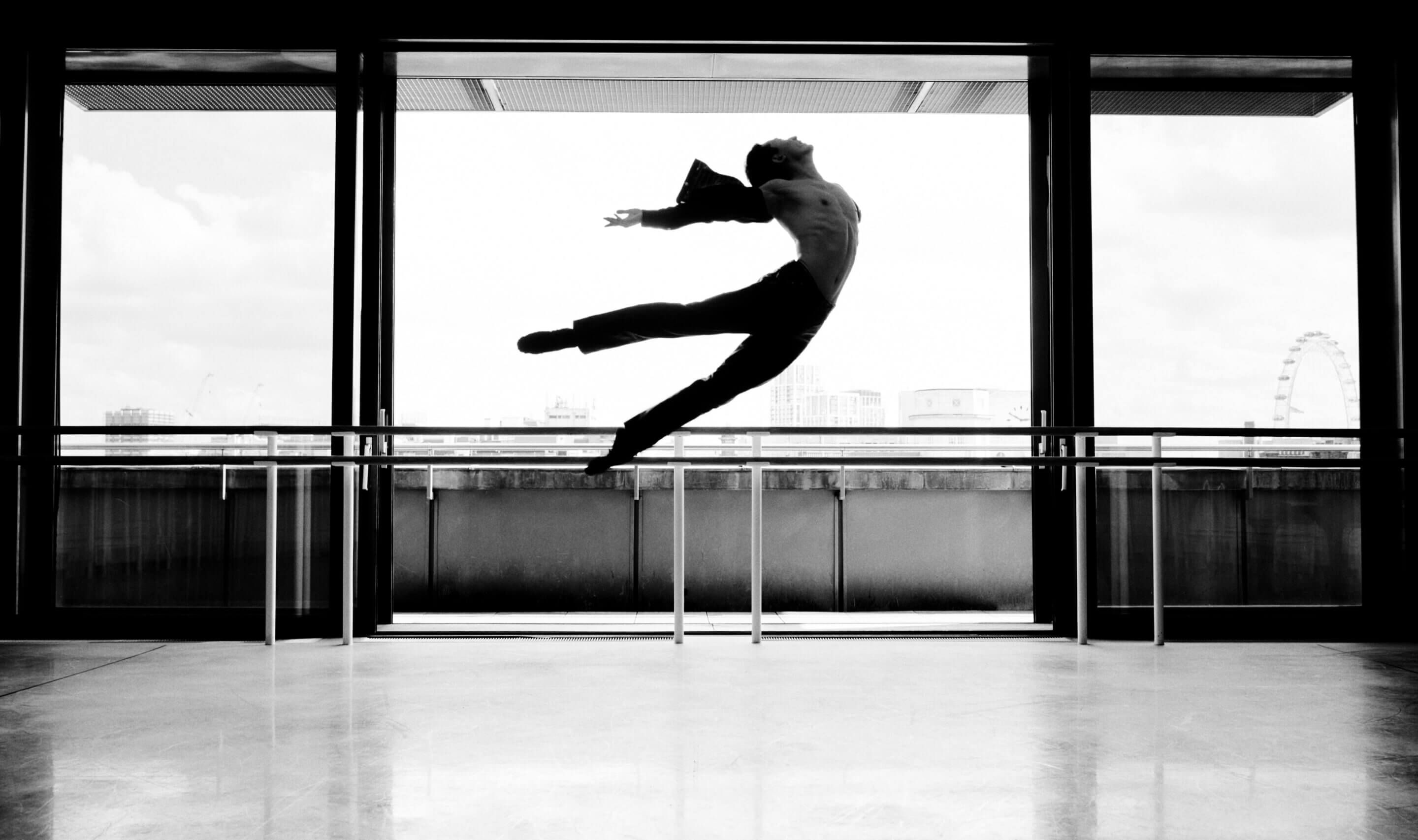 A black and white photograph showing a man dancing ballet and jumping in the air.