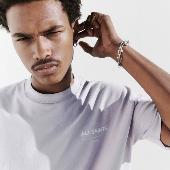 Closeup photograph of a male model wearing a lilac AllSaints t-shirt, a chain bracelet and a hoop earring.