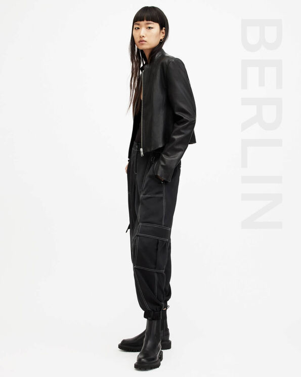 Portrait of a model wearing a black zip up leather jacket with with black cargo trousers and black boots with BERLIN written on the right hand side.