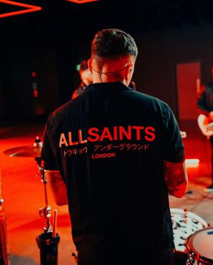 Interprète se tenant de dos et portant un t-shirt manches courtes au logo AllSaints.