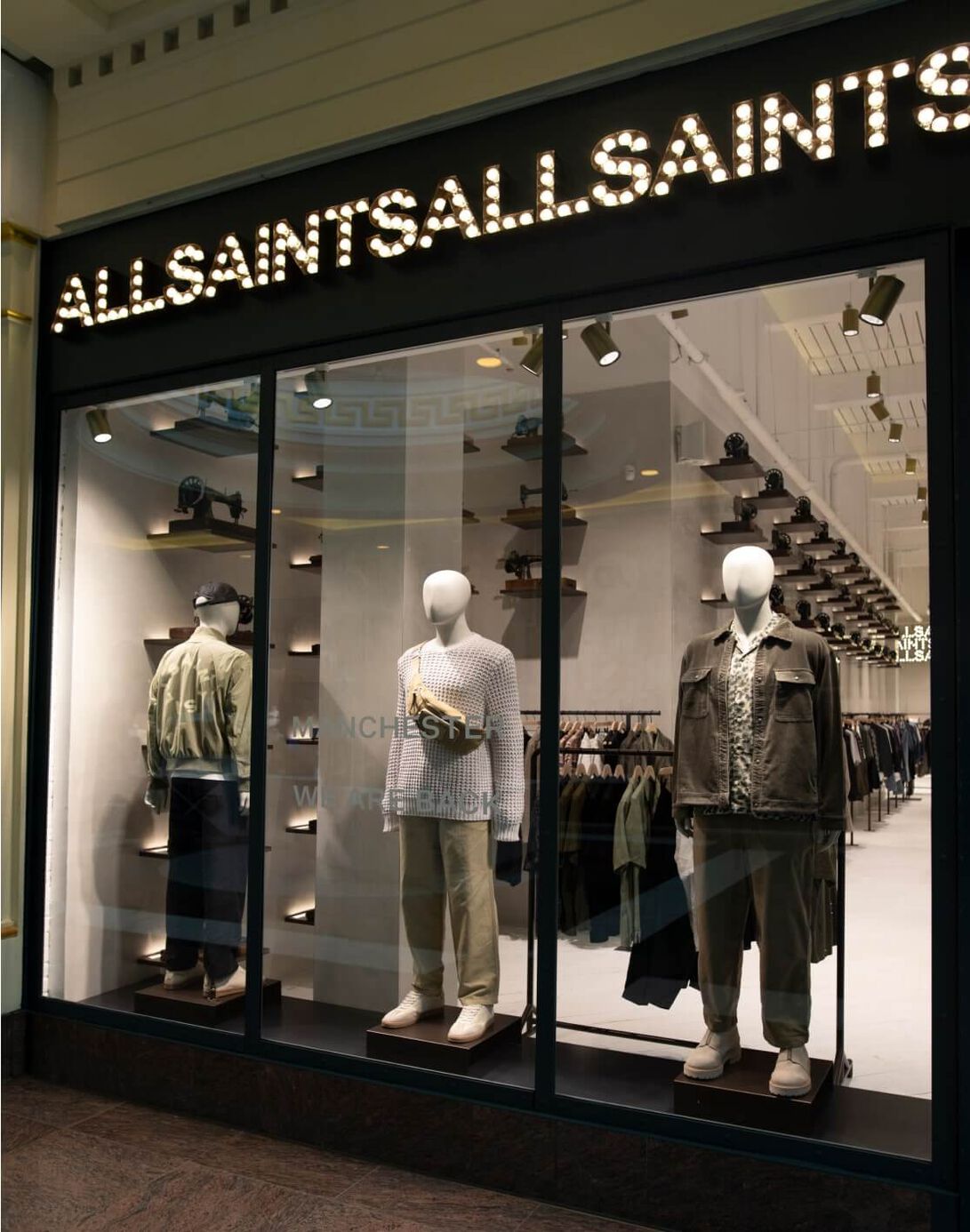 Photograph showing the main display window to our Trafford store in manchester, with mannequins and ALLSAINTS written in light bulbs.