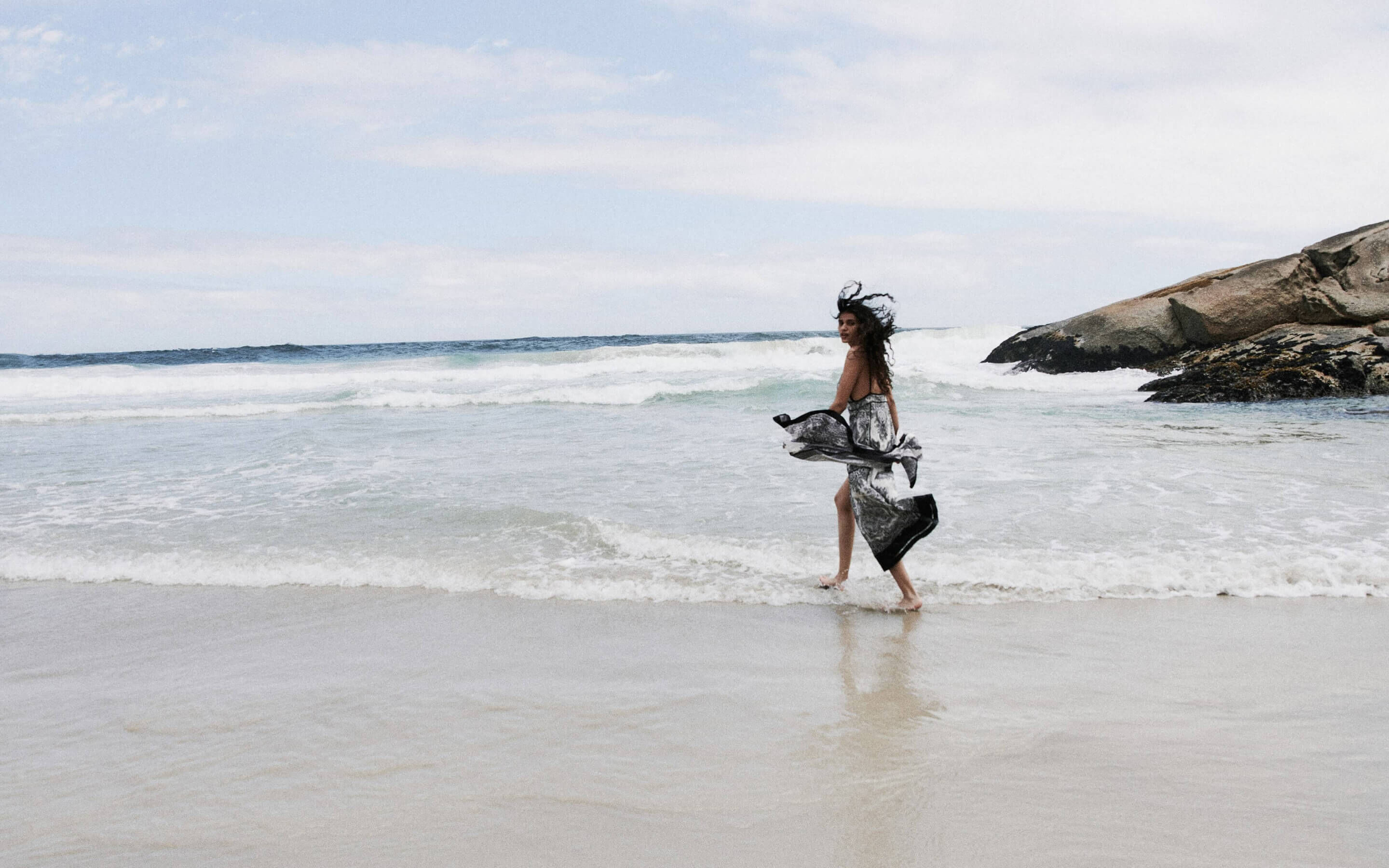 Une femme marchant à la plage portant une robe noire et blanche