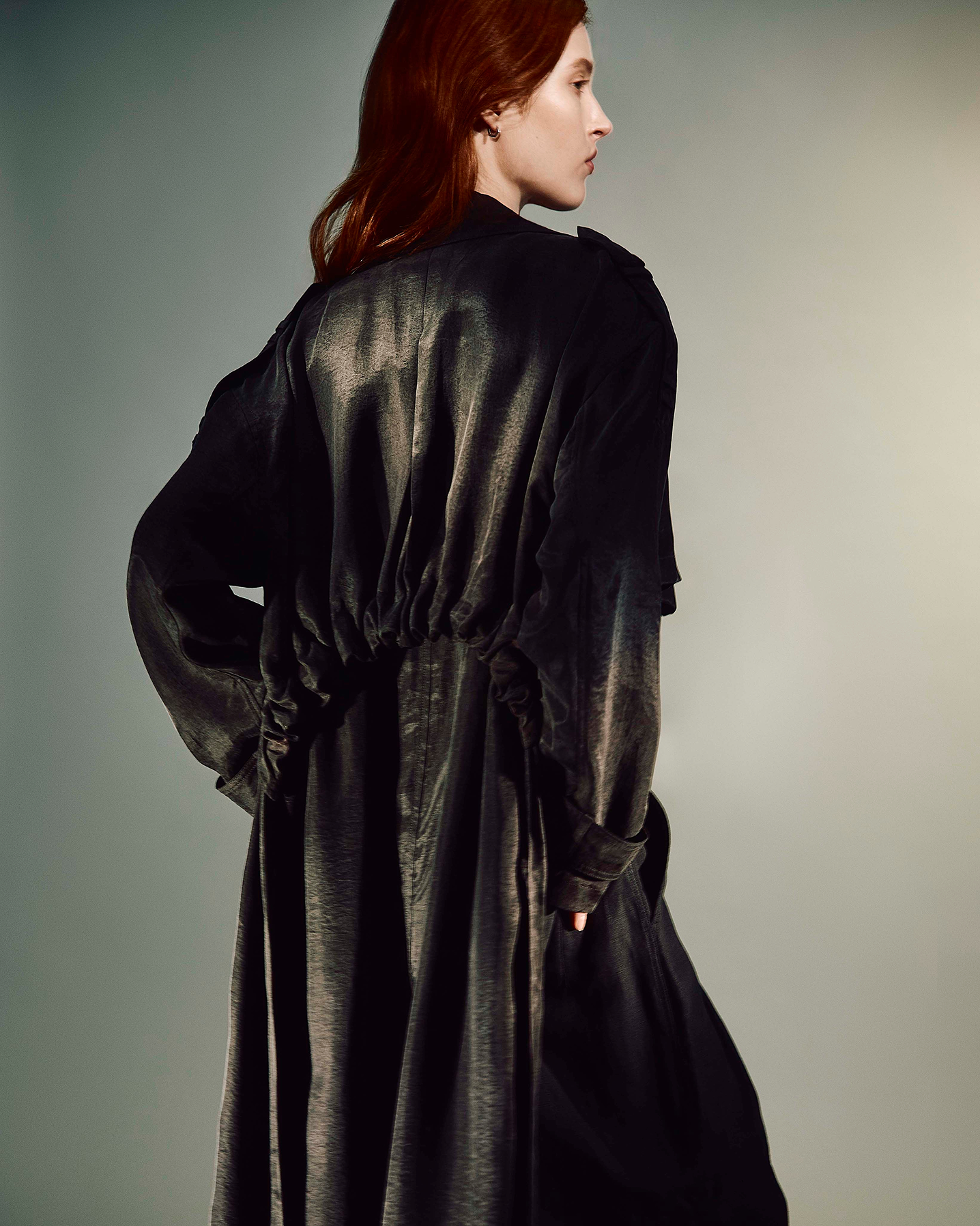 Women facing away from the camera wearing a black trench coat with a grey background