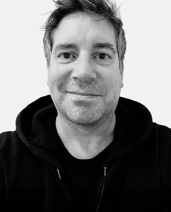 A black and white headshot of a man wearing a black hoodie in front of a white background