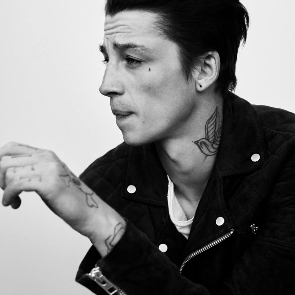 Black and white image of a male model with tattoos and a leather jacket