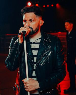 Singer sings into a microphone wearing a biker jacket over a striped jumper..