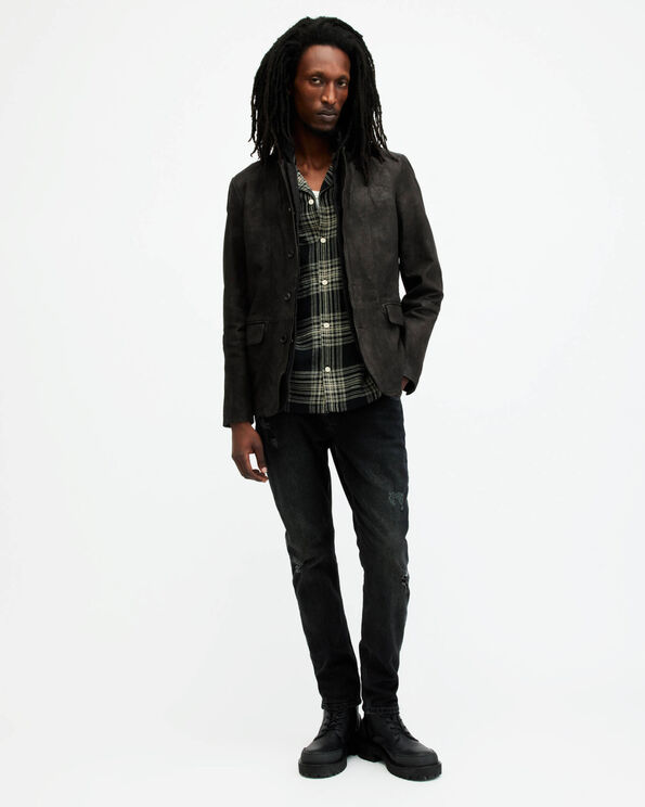 Portrait of a male model wearing a black leather blazer over a checked black shirt, with jeans and black leather boots.