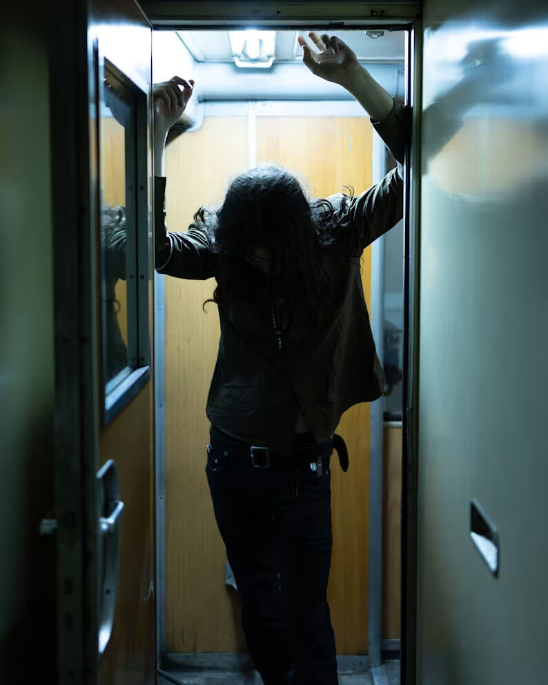 Person standing inside a train carriage with arms raised in an AllSaints editorial photograph