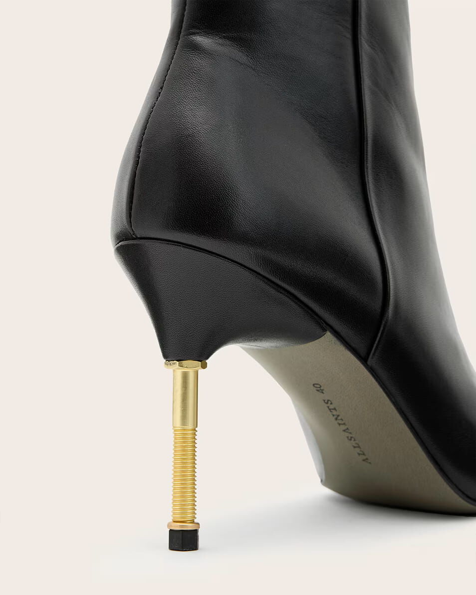 Close up shot of the gold heel on a black leather high heeled boot.