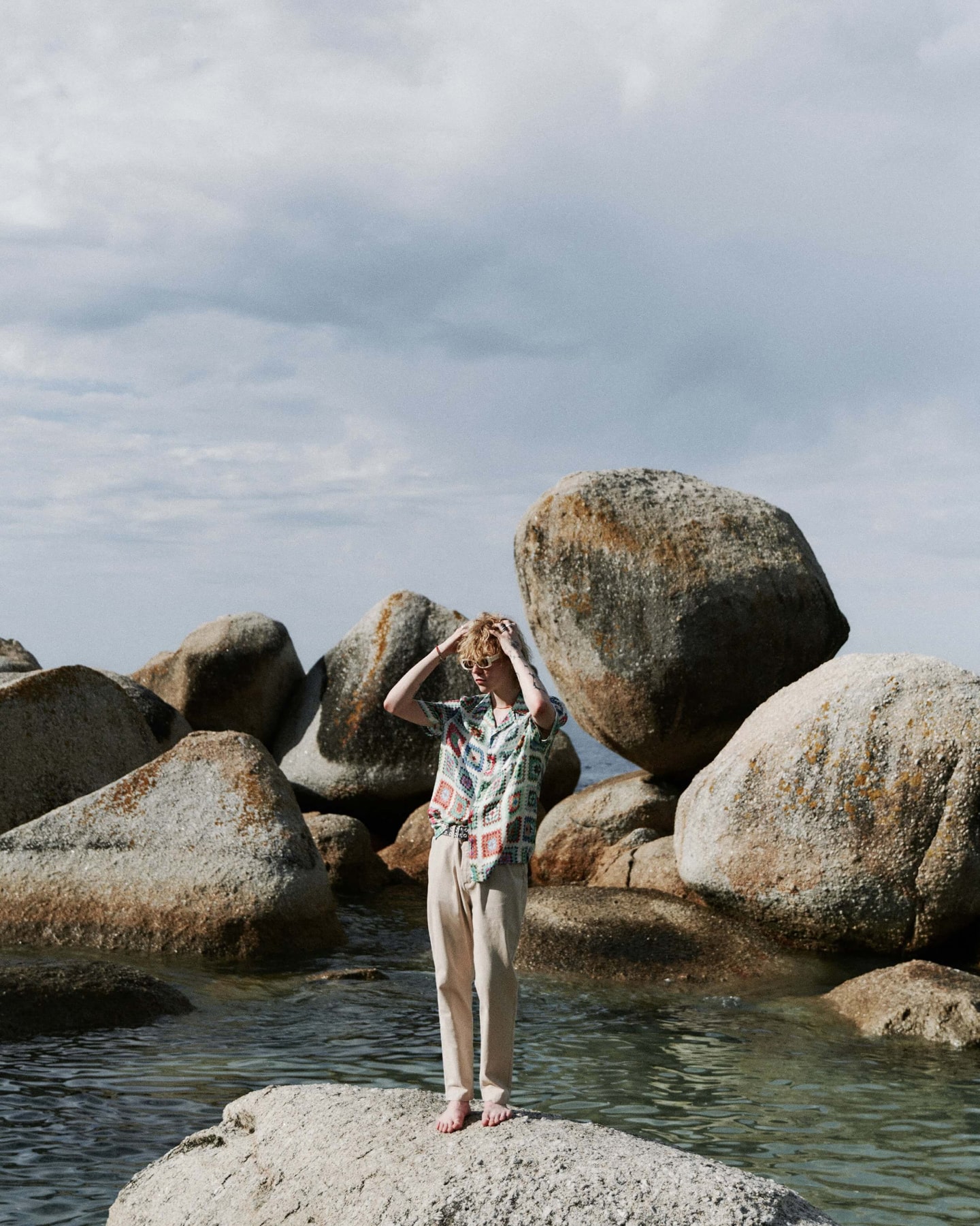 Man standing on rocks by the sea, wearing items from our latest collection.