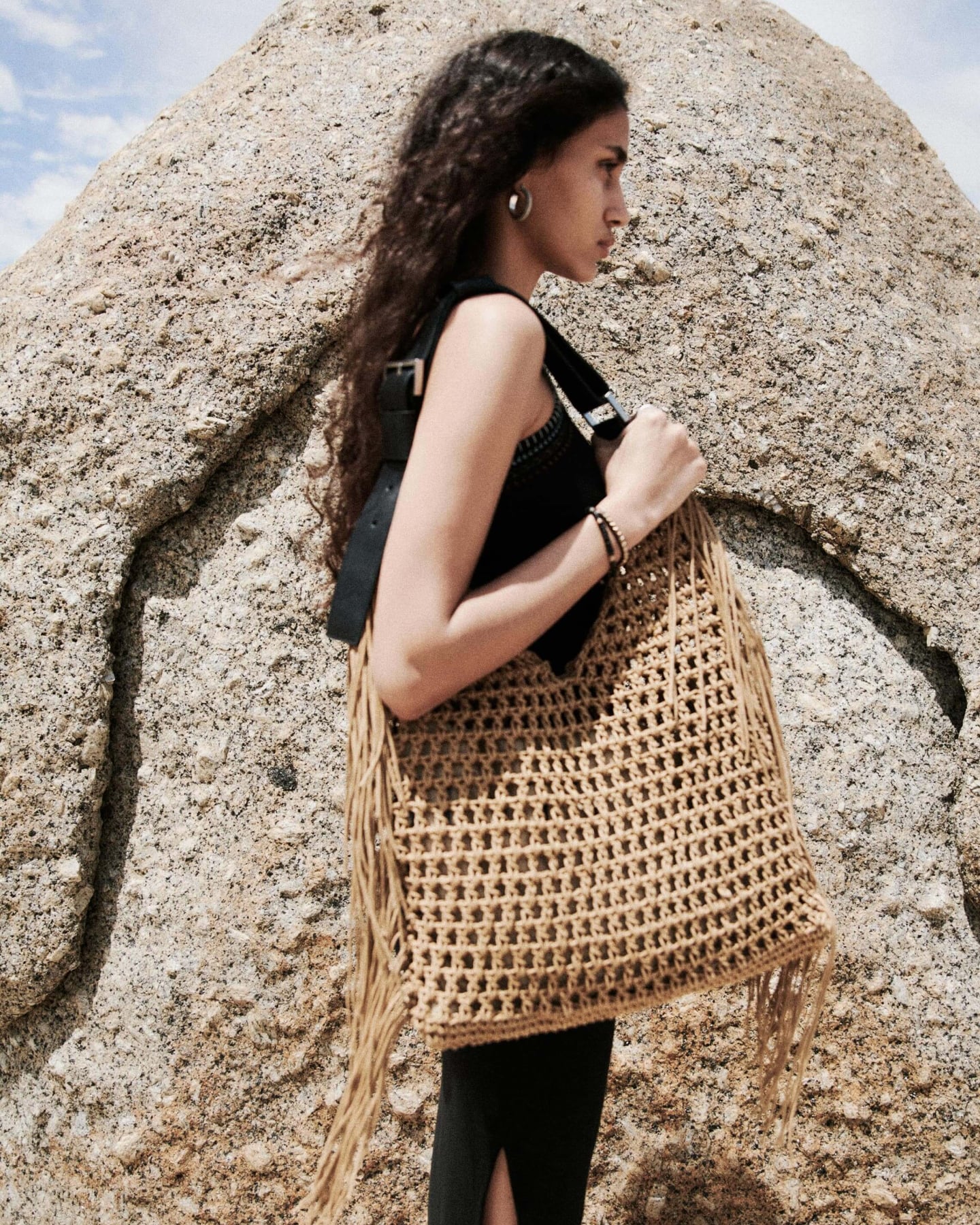 Femme portant une robe noire et un sac en crochet se tenant devant un grand rocher.