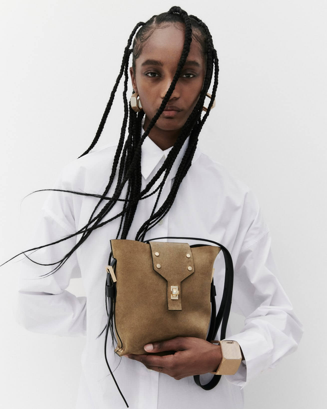 Woman wearing a white shirt, with suede leather shoulder bag and statement earrings and bracelet.