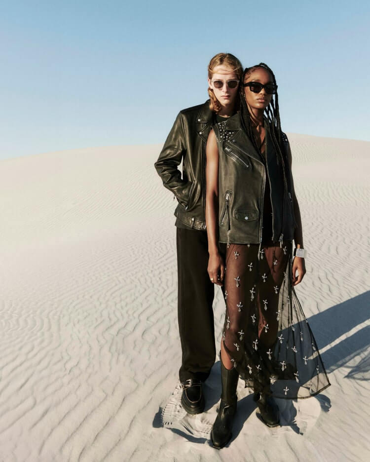 Man and woman stood in black clothing, leather jackets and sunglassed in the desert.